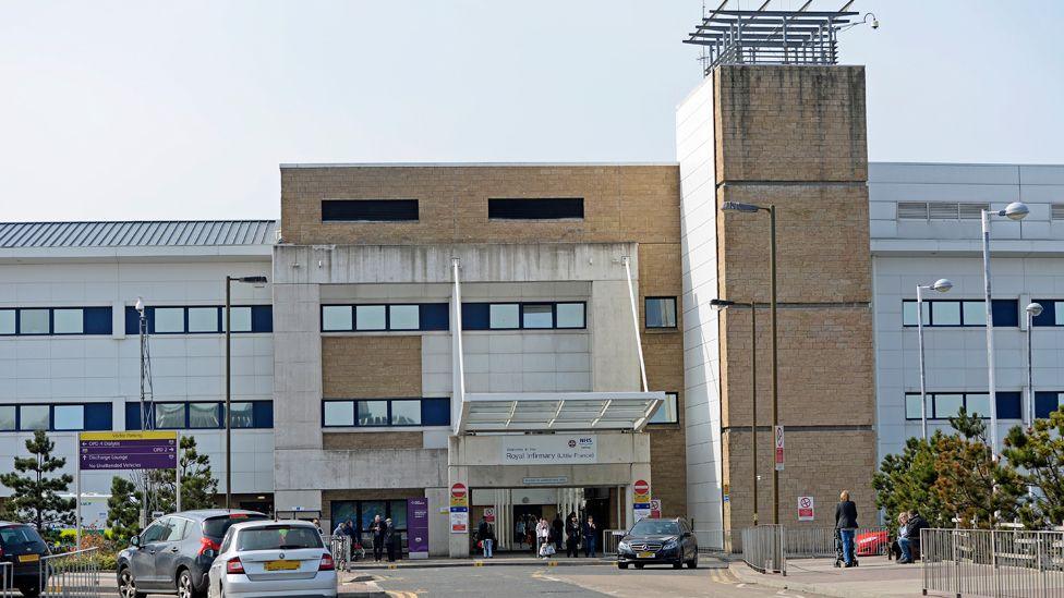 The outside of the Royal Infirmary of Edinburgh, with a number of cars and pedestrians.