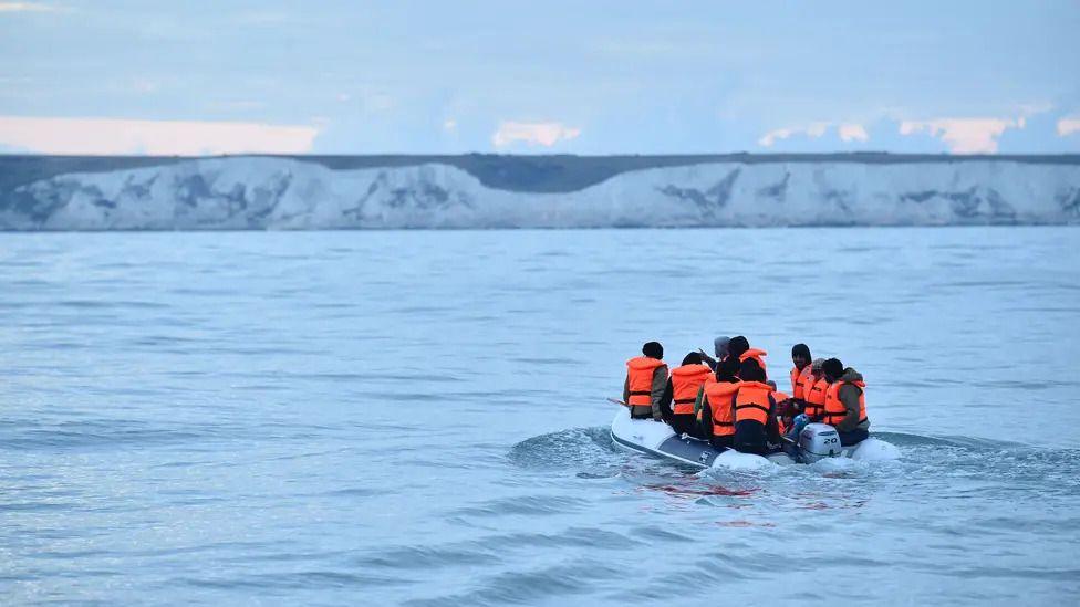 A group of people on an inflatable boat with the White Cliffs of Dover in the background.