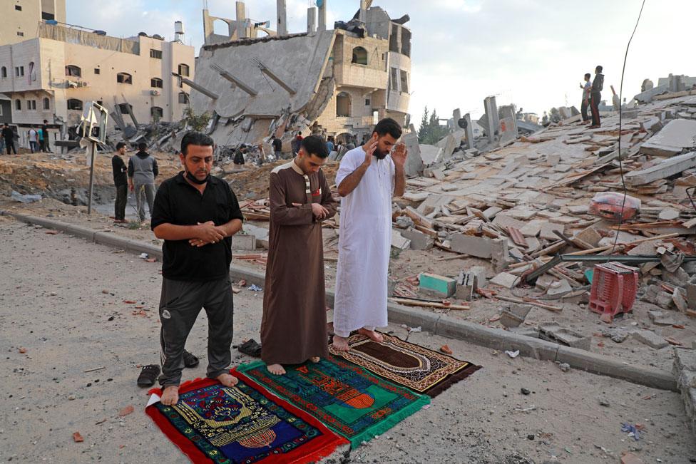 Muslim men perform the morning Eid al-Fitr prayer with destroyed buildings behind them in Beit Lahia in the northern Gaza Strip