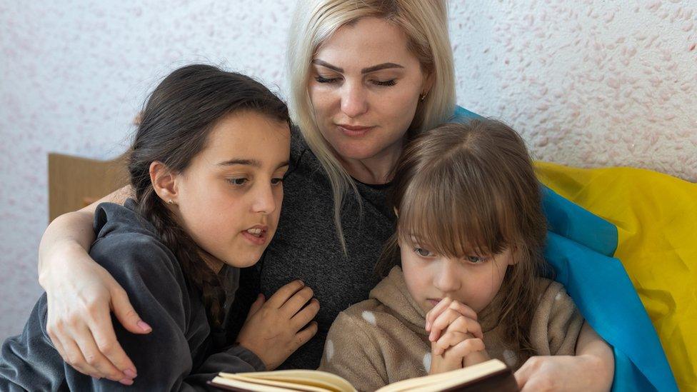 Mother and daughter reading a book with a flag of Ukraine on a bed, stock photo