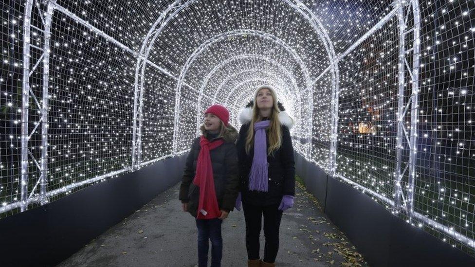 People stand in an archway which forms part of the illuminated trail through Kew Gardens after-dark landscape.