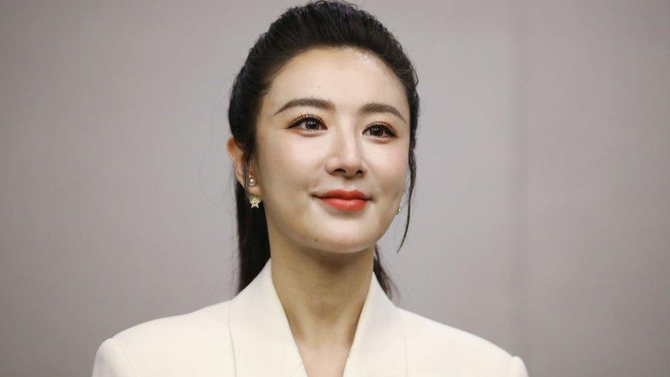 Viya Huang Wei seen in front of beige background, wearing a white suit jacket at product expo in May 2021