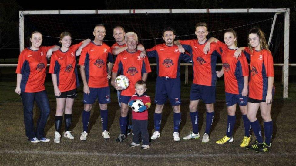 Peter carrying a football stands in the middle of a Webster family football team picture