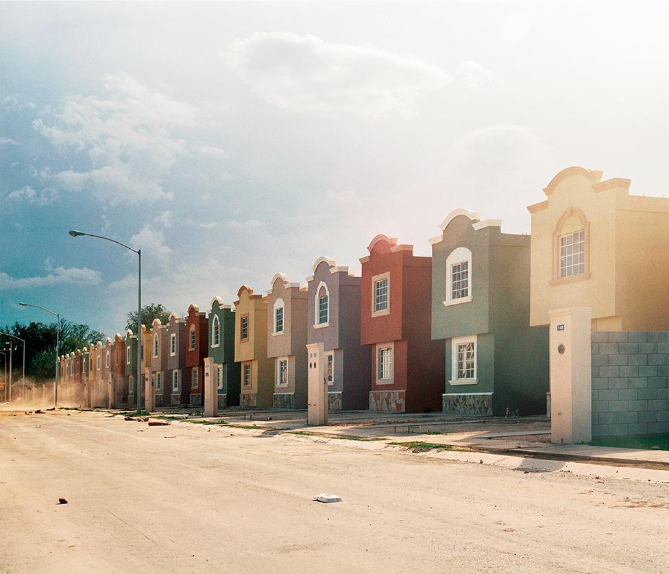 A photo by Alejandro Cartagena showing a line of colourful homes on an empty street