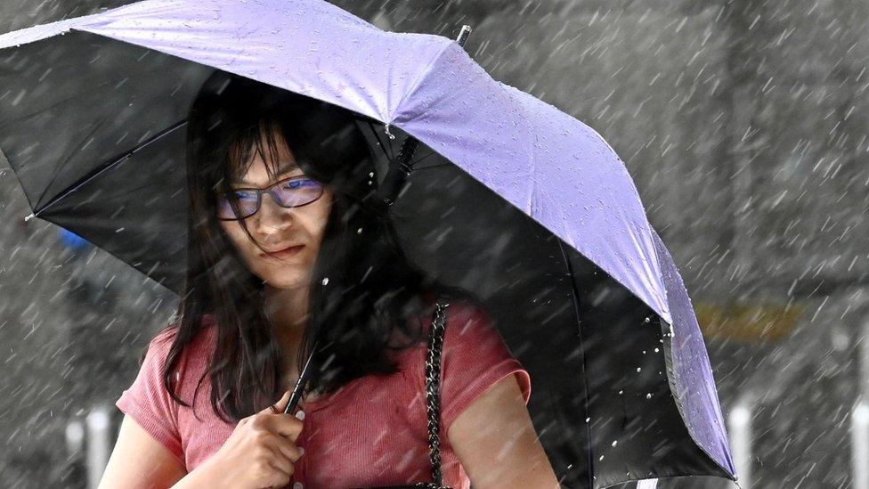 A woman shields herself with an umbrella as she walks in New Taipei City in rain brought by Typhoon Lekima as it passes northeastern Taiwan on August 9, 2019