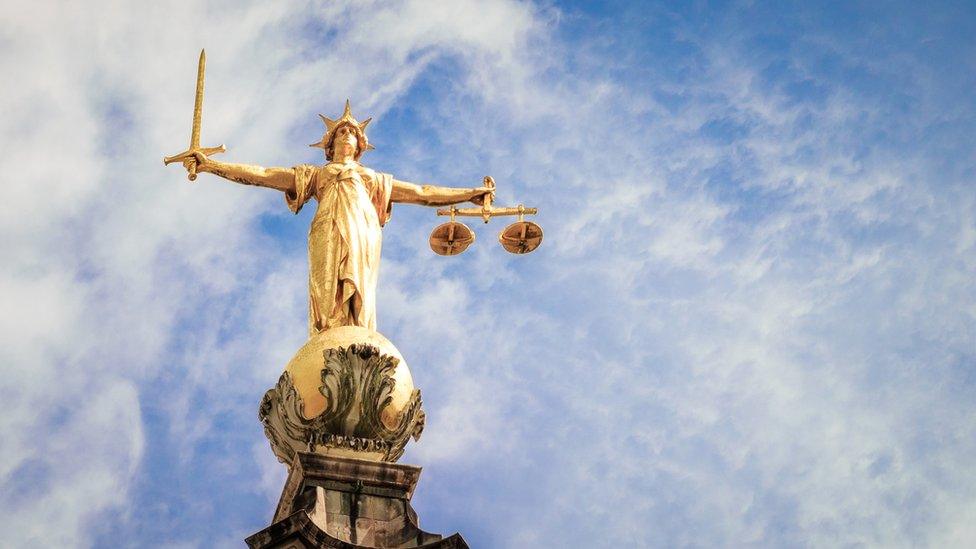 A telephoto image of the statue of Lady Justice, holding a sword and weighing scales