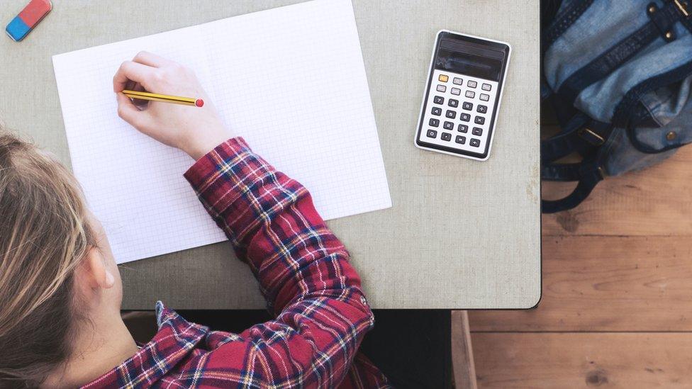 A schoolgirl writing on a piece of paper with a calculator