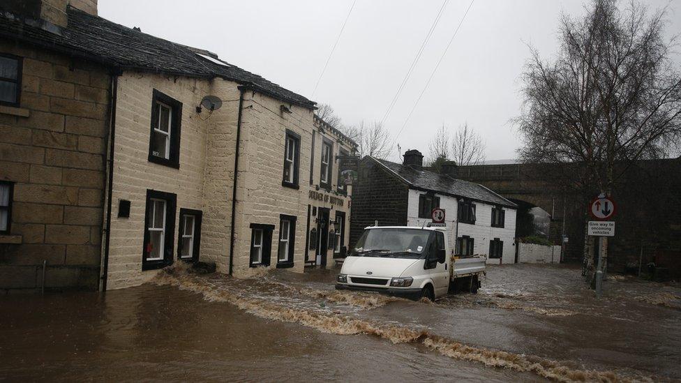 A vehicle drives through flood waters at Mytholmroyd in Calderdale