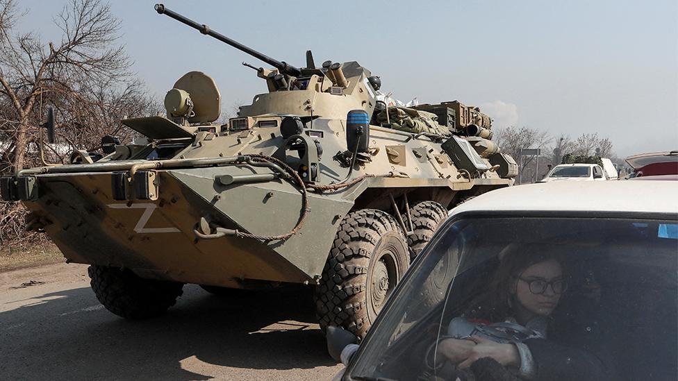 A refugee waits in a car as an armoured personnel carrier of pro-Russian troops drives out of a checkpoint in the course of Ukraine-Russia conflict in the besieged southern port city of Mariupol, Ukraine, 24 March 2022.