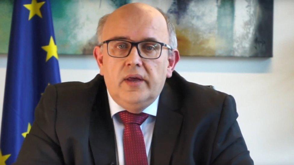 Wojciech Wiewiórowski is seen looking into the camera in this still frame, with an EU flag behind him