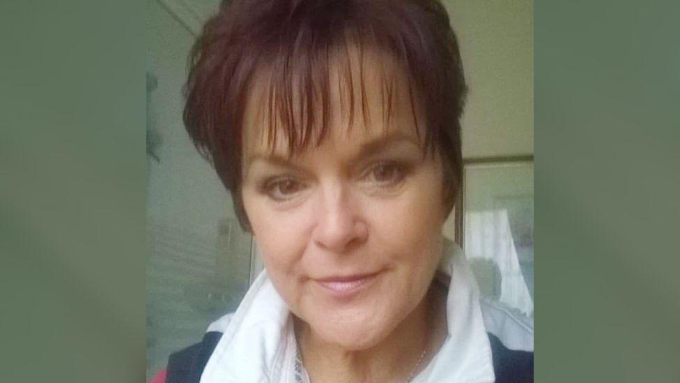 A selfie of Melanie Wellings before the surgery or cancer diagnosis. She is wearing a white collared shirt, has short dark hair in a pixie cut, and is smiling at the camera.