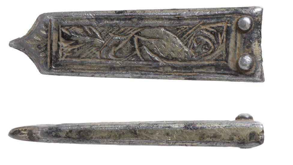 Two views of a medieval silver strap-end. It is rectangular in shape with a flat top, with two silver circles soldered at the top, narrowing slightly along its body until it ends in a point.  The front side is engraved with a human-headed bird. The other view is of its narrow side, wider at the top and narrower at the bottom