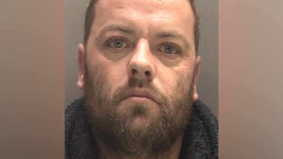 Police mugshot of Martin Taylor, who has a brown facial hair and is looking at the camera with a blank expression