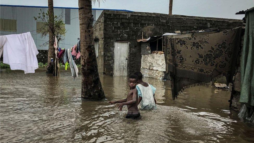 Children walk down a flooded road while sheets and covering are hung out to dry