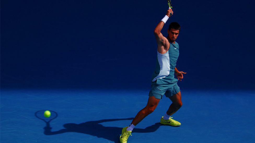 Tennis player Carlos Alcaraz hitting the ball during the 2025 Australian Open, with his shadow appearing as though it is hitting the ball.