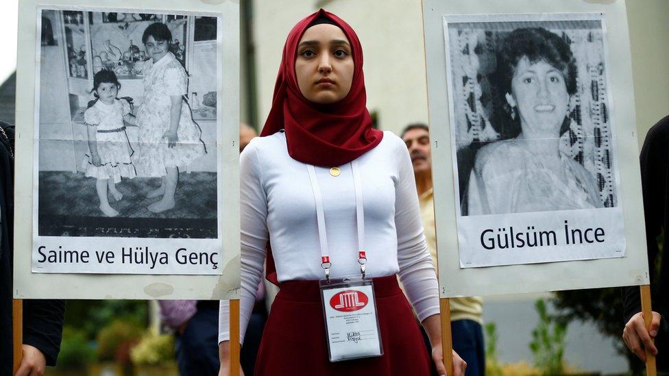 A woman holds pictures of victims during a silent remembrance commemorating the 25th anniversary of an arson attack killing two Turkish women and three girls by right-wing extremists in Solingen