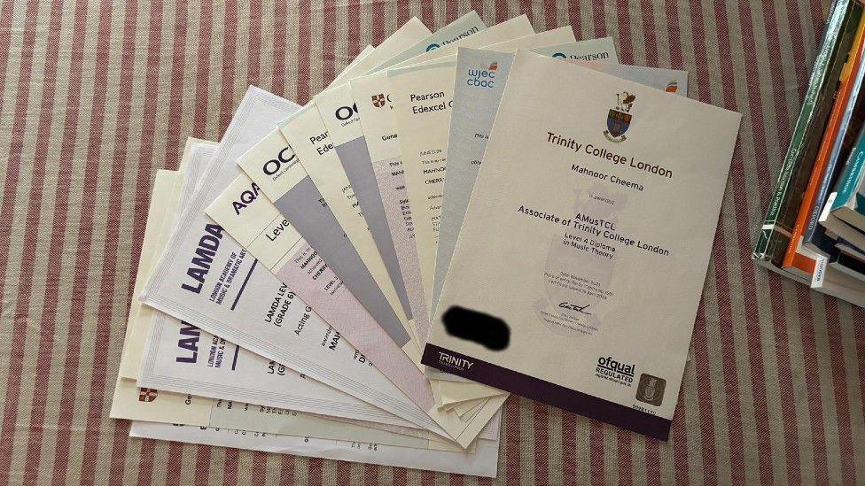 A pile of A-Level exam certificates, fanned out on top of a red and white stripy tablecloth.