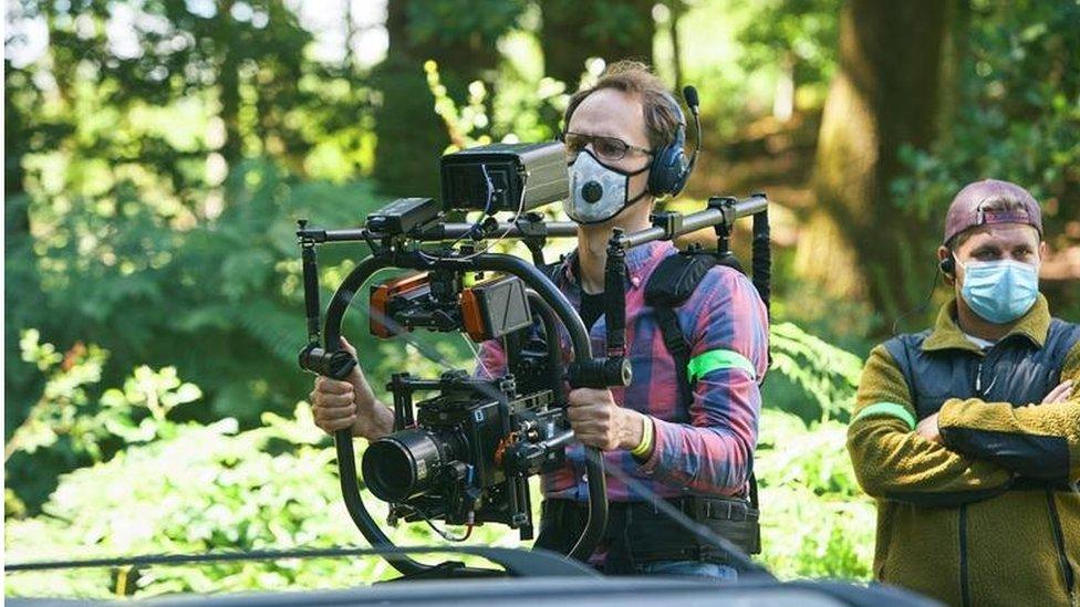 A camera operator wearing a mask holding a camera