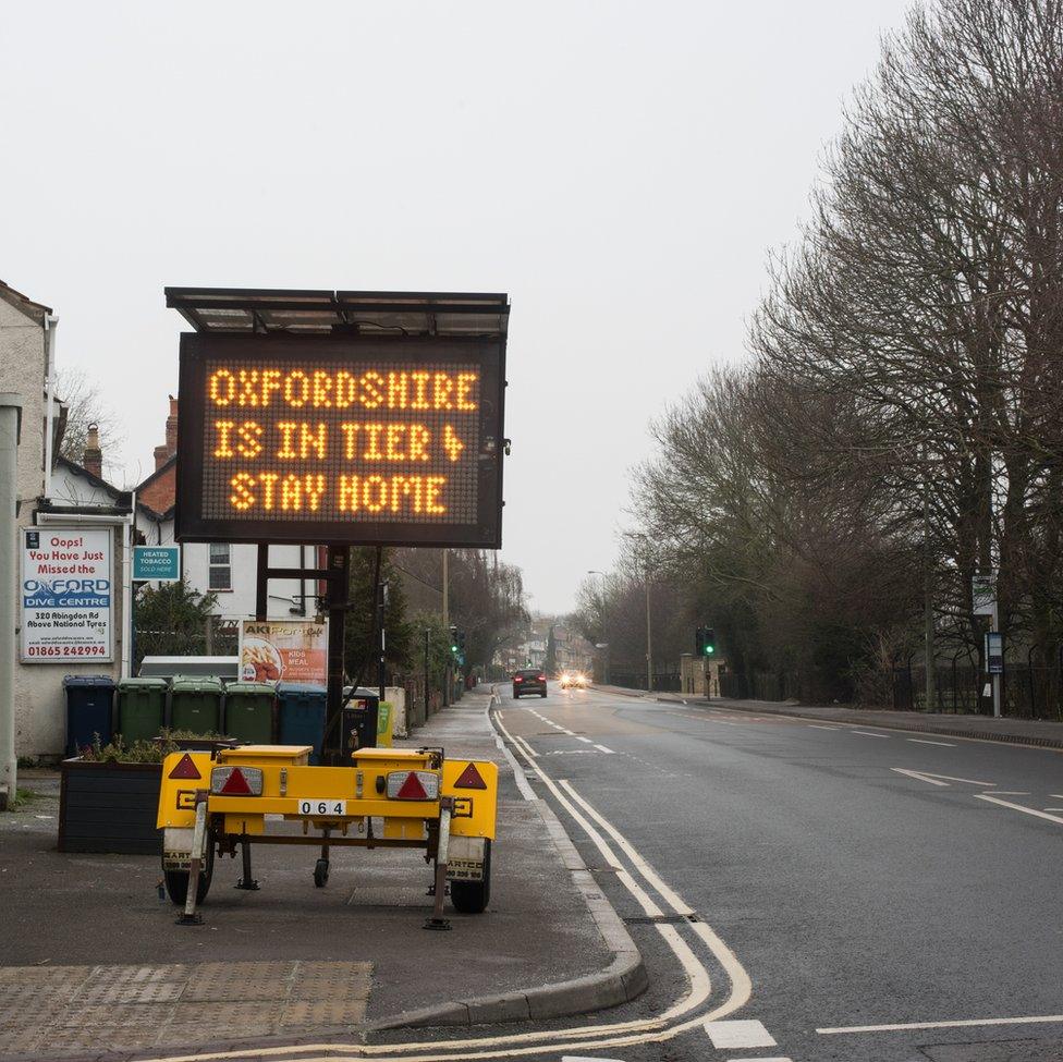 An image of a sign instructing people to stay at home next to a main road