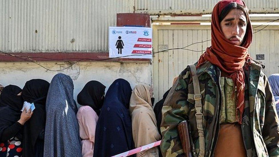 A Taliban fighter stands guard as women wait in line during a World Food Programme food distribution in Kabul