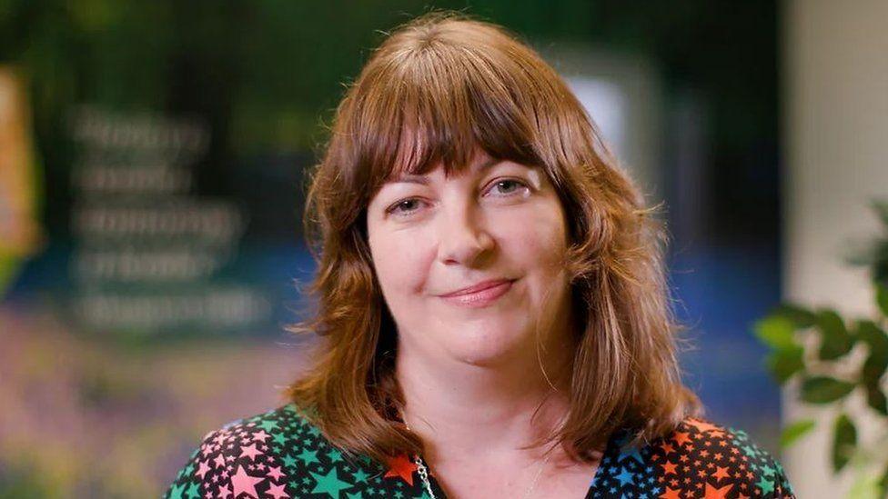 Niamh Sweeney with mid-brown shoulder-length hair and a fringe wearing a black top with green, pink, blue and red stars