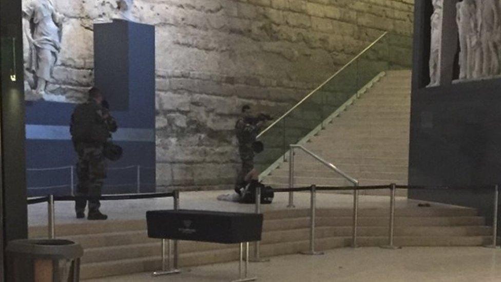 The body of a man lays on the floor as two soldiers guard him in the Louvre museum, on 3 February 2017 in Paris.