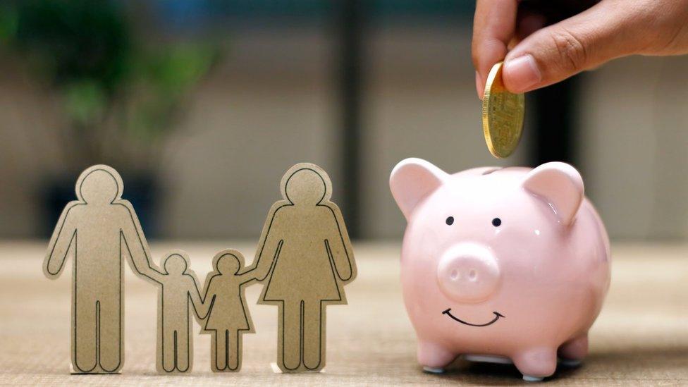 Hand putting money coin into piggy bank and family paper on table