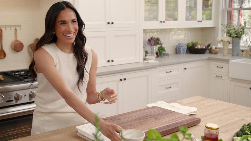 A promotional photo released from the With Love, Meghan programme shows the smiling duchess in a bright and spacious kitchen. She wears a sleeveless cream top and skirt.