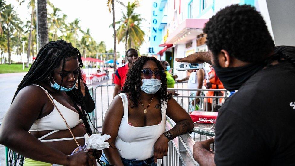 A security guard checks the temperature of a woman at the entrance of a restaurant on Ocean Drive in Miami Beach, Florida, 24 June 2020