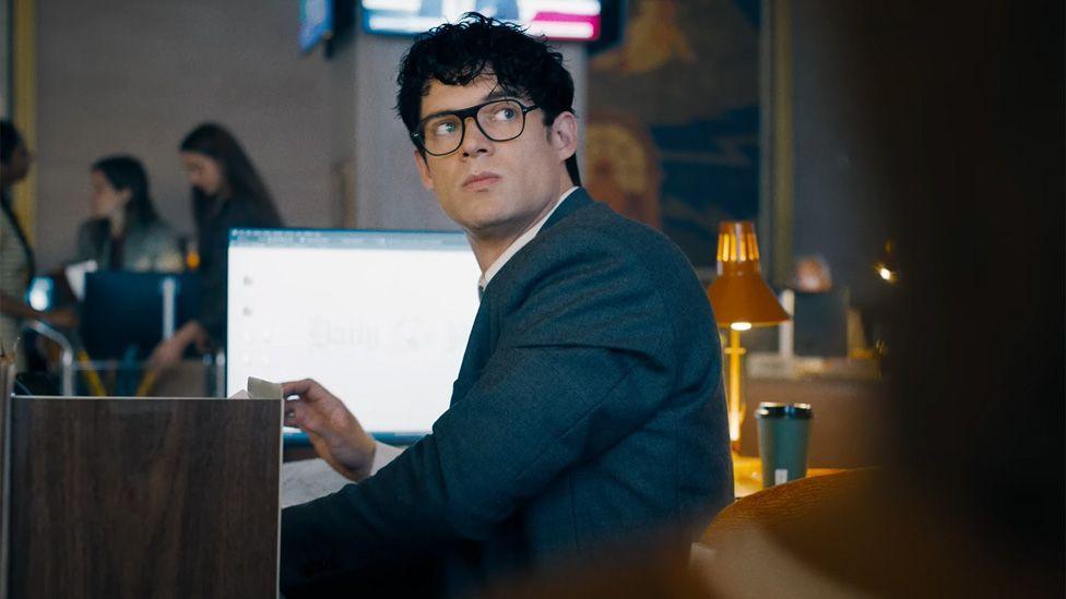 David Corenswet as Clark Kent sitting at a desk in the Daily Planet office in a still from the trailer.