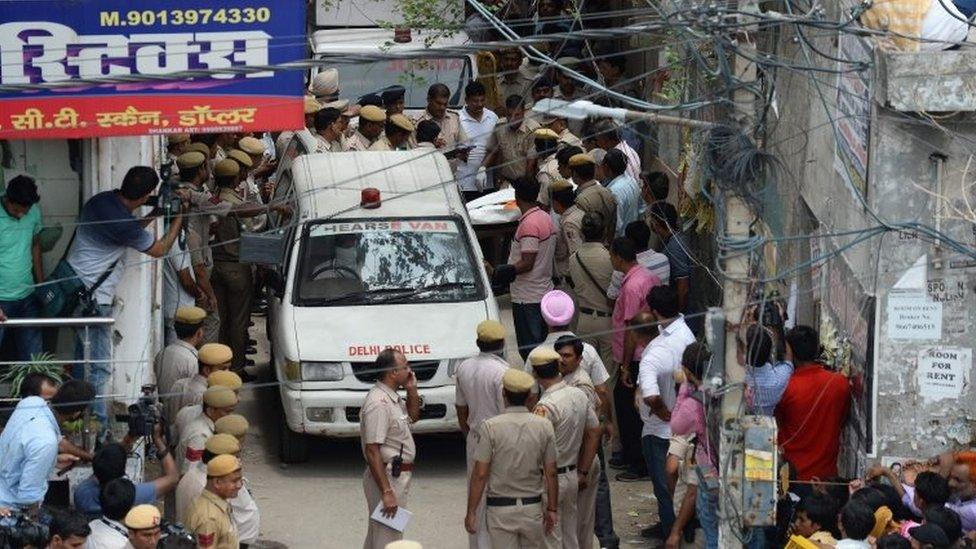 Indian policemen carry the body of a victim into a hearse van after 11 family members were found dead inside their home in the neighbourhood of Burari in New Delhi on July 1, 2018.