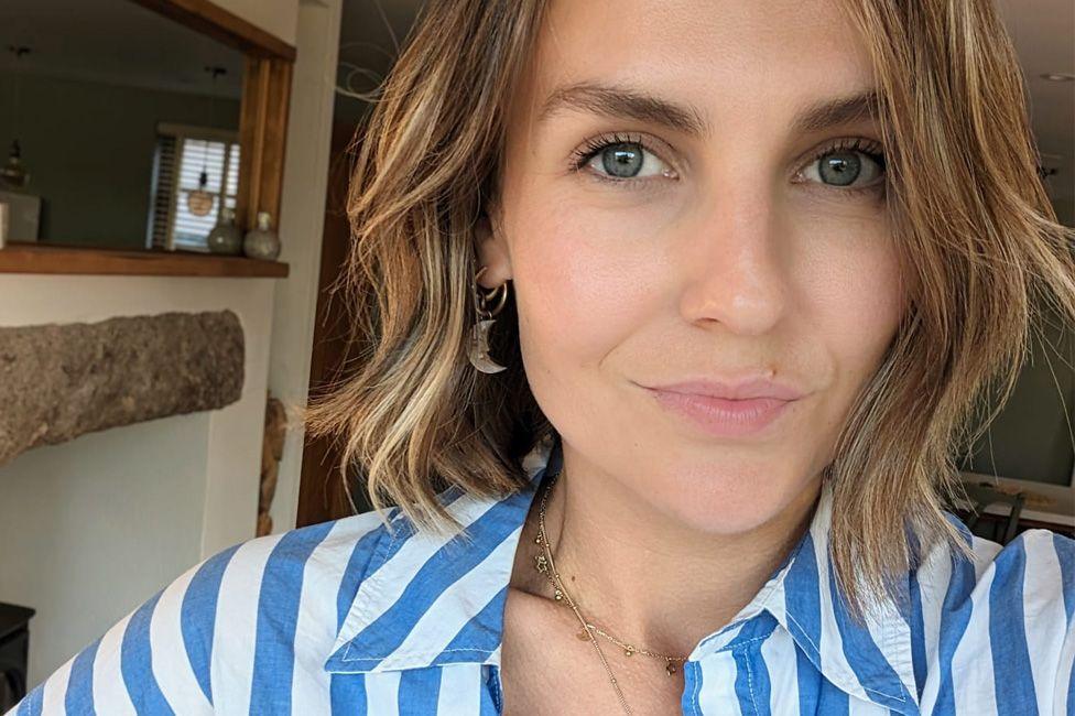 Olivia Lott, a 30-year-old woman, takes a selfie indoors while looking at the camera and wearing a striped blue and white shirt