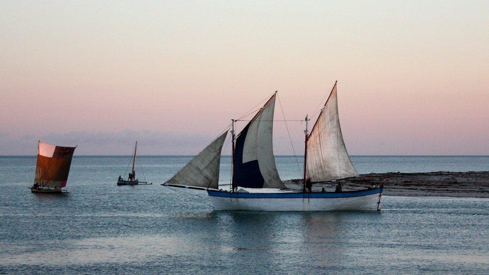 A schooner sails from the coast at dusk