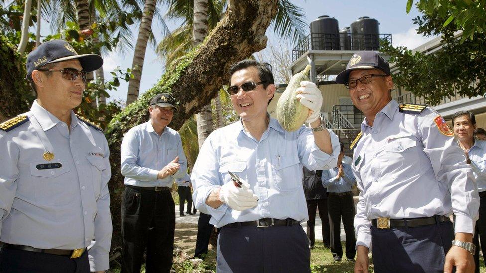 President Ma Ying-jeou holding up a fruit, and flanked by officials