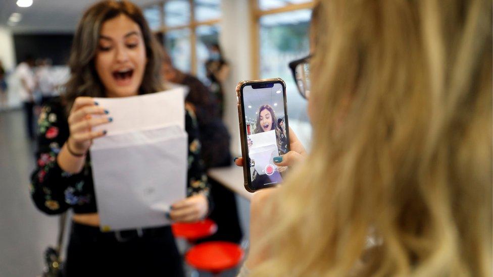 A girl photographs another one looking at her results