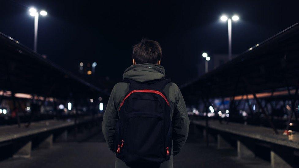 Rear view of young boy carrying rucksack down a street at night