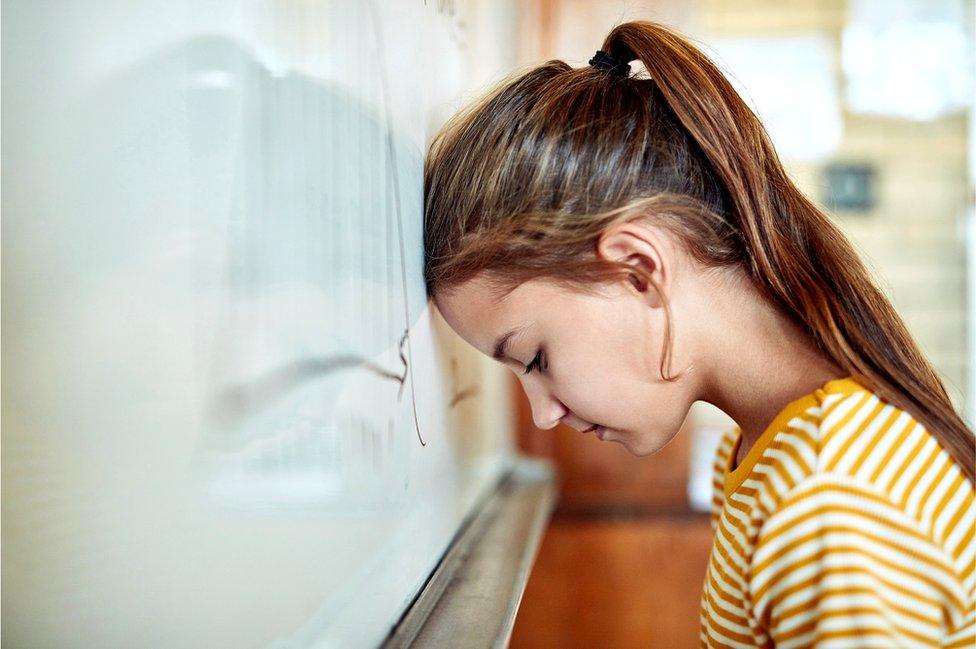 girl leans head on classroom wall