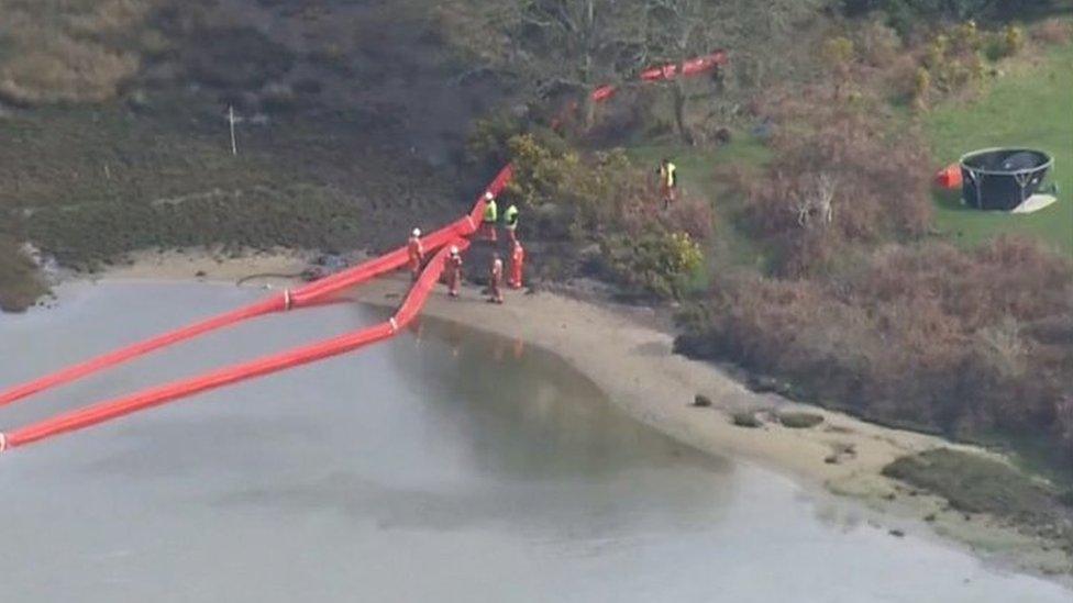 Workers and a boom in the water at Poole Harbour