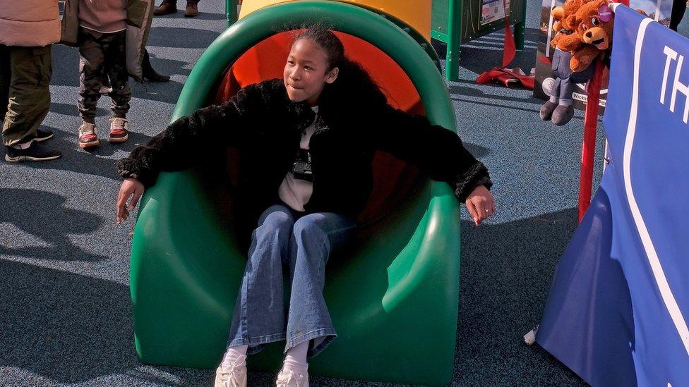 Girl (Mia) in dark top sitting at the bottom of a green and yellow tube slide