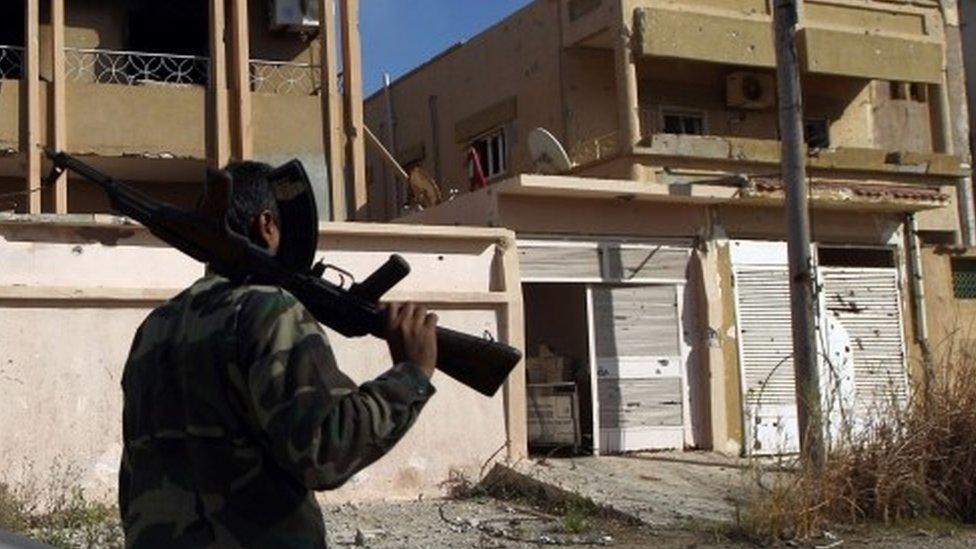 A fighter loyal to Libya's internationally recognised government walks along damaged a street in Benghazi (23 February 2016)