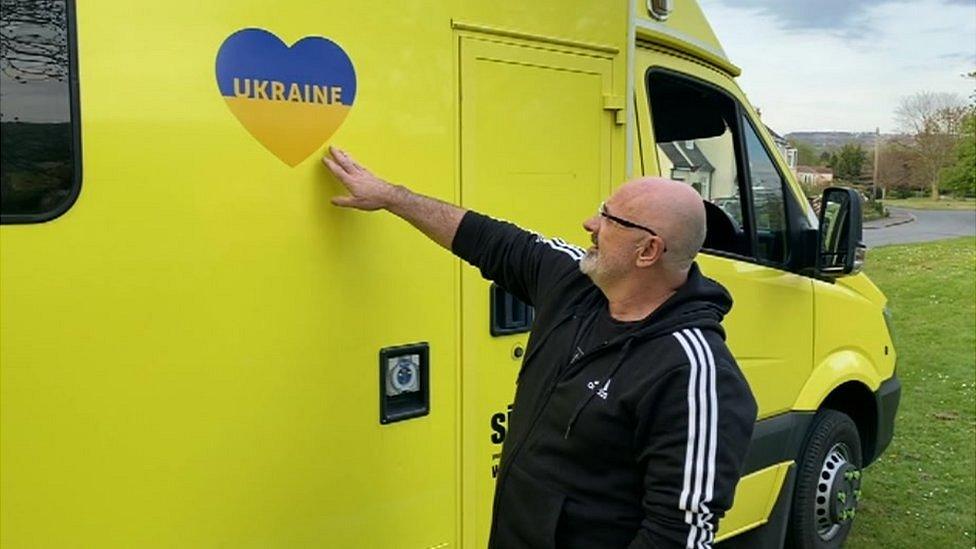 Bruce Byron reaches to touch an ambulance which has a Ukraine flag in a heart shape on the side