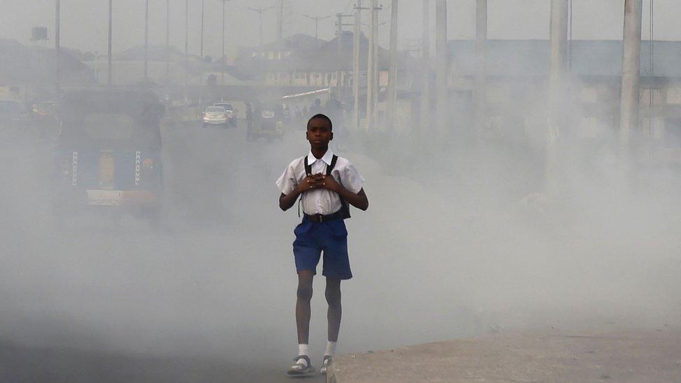 A school boy walks past smoke and fumes emitted from a dump in the city of Port Harcourt.