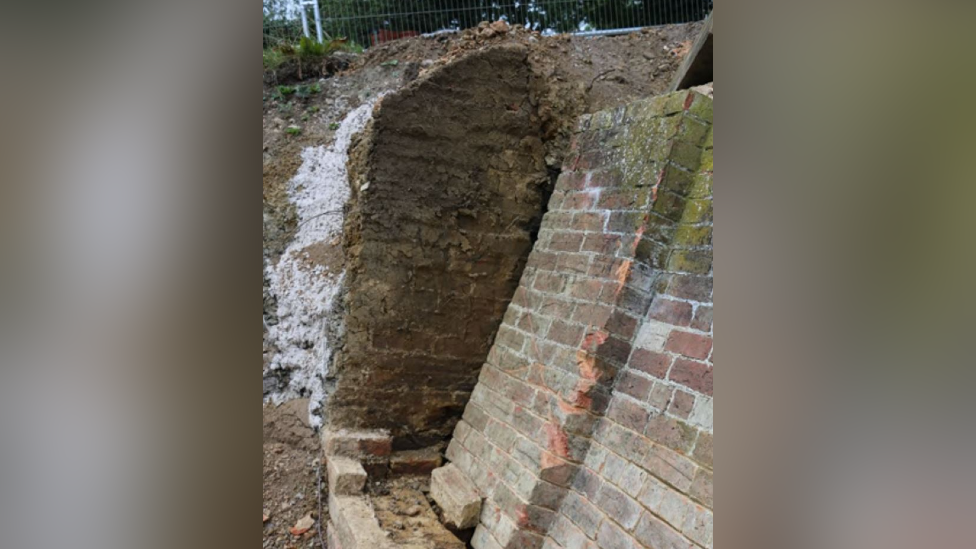 Image of a collapsed brick wall along a canal path