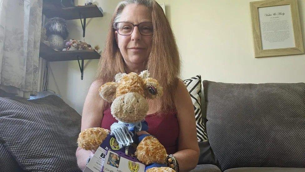 Vickie Hall sat ona sofa with her cuddly toy giraffe and certificates