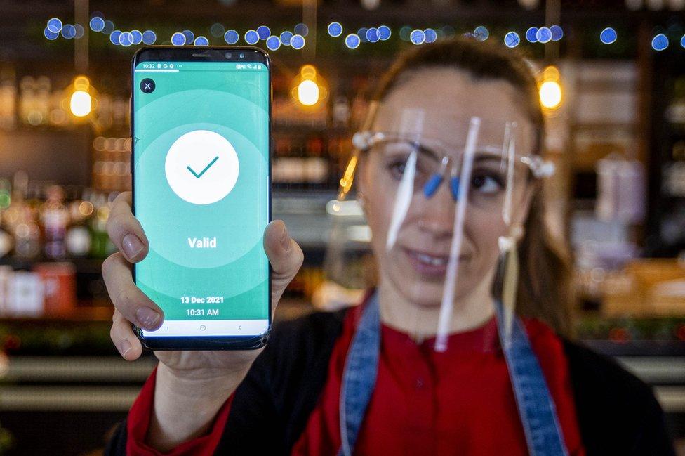 A bar worker holding a phone which is displaying a Covid-19 vaccine certificate