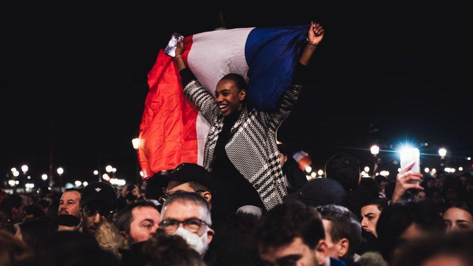 A happy France fan with a flag sits on someone's shoulders