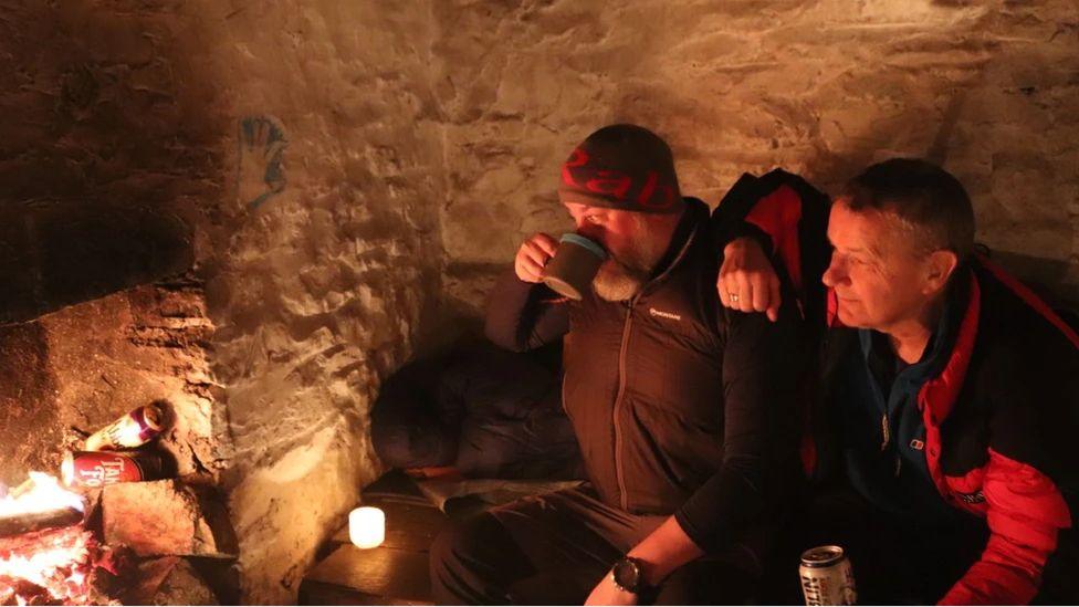 Gareth a'i ffrind yn treulio'r noson yn y bothy ar droed Arenig Fawr, ac yn cadw'n gynnes o flaen tanllwyth o dân