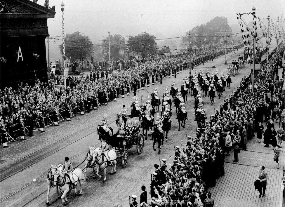 The Queen and Prince Philip ride in a carriage along Princes Street while people line both sides of the road