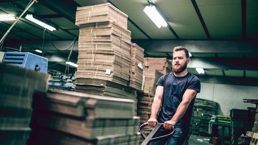 Tired Worker Pushing Cardboard Carton Planks On Transportation Cart on Night Shift