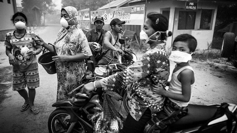 Locals in Bereng Bengkel go about their daily lives wearing haze masks